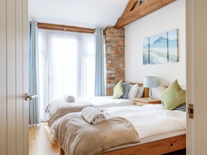 Habitación de hotel con dos camas, una pared de ladrillo, un cuadro y una viga de techo de madera.