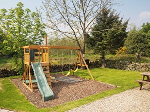 Un parque infantil con un tobogán, columpios y una casita de madera.