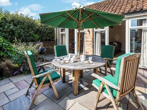 Une table ronde en bois, entourée de chaises, un parasol vert et un mur de briques en arrière-plan.