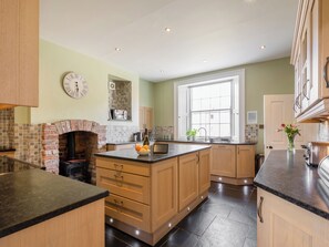 A kitchen with a brick fireplace, wooden cabinets, a large window, and a clock on the wall. - Thirley Cotes Farmhouse (Harwood Dale, near Scarborough)