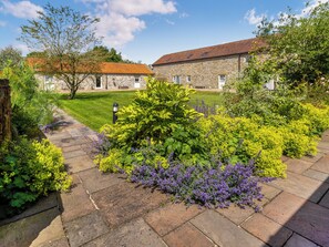 A stone building with a red-tiled roof, surrounded by a well-maintained garden with various plants and a stone pathway. - Thirley Cotes Farmhouse (Harwood Dale, near Scarborough)
