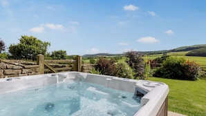 Een hottub met een stenen muur en houten poort, omgeven door groen en een prachtig landschap.