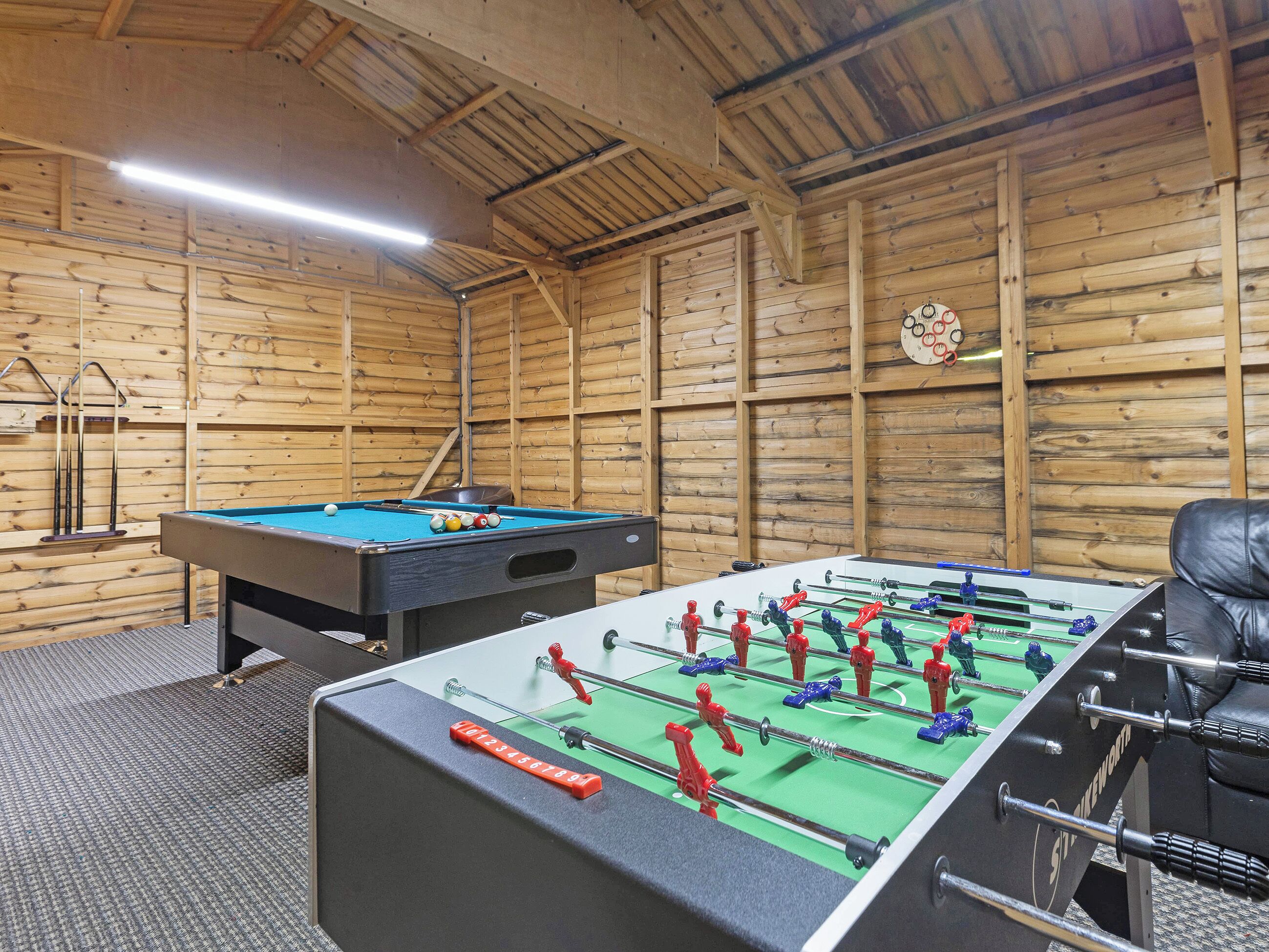 Een kamer met een pooltafel, een tafelvoetbaltafel en een biljarthouder.