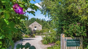 Een stenen vakantiehuisje met een grindpad dat er naartoe leidt, omringd door weelderig groen en een bordje met de tekst 'Thirley Cotes Farm Luxury Self Catering Cottages'.