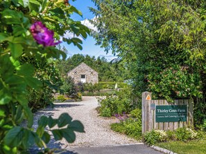 A stone cottage with a gravel path leading to it, surrounded by lush greenery and a sign indicating 'Thirley Cotes Farm Luxury Self Catering Cottages.' - Thirley Cotes Farmhouse (Harwood Dale, near Scarborough)