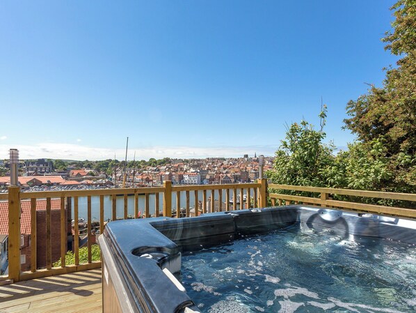 Ein Whirlpool mit einer Holzterrasse und Blick auf eine Stadt am Wasser.