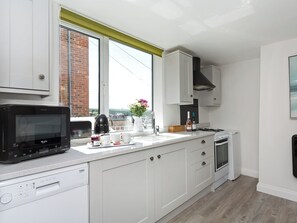 A modern kitchen with white cabinets, a built-in microwave, a stove, and a window with a view of the city. - 1 bedroom accommodation in Whitby (Whitby)