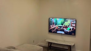 Uma sala de estar com televisão de tela plana na parede, uma mesa de centro de madeira e dois sofás bege.