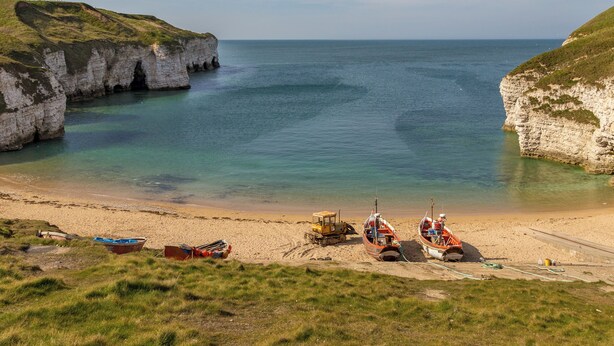 Ein Küstenstrand mit Klippen, Booten und einem Traktor im Sand.