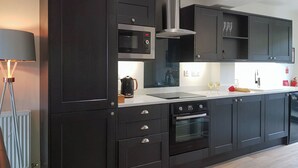 A modern kitchen with dark cabinetry, a built-in microwave, a stainless steel range hood, a double oven, and a countertop with a kettle and wine glasses. - 3 bedroom accommodation in Whitby (Whitby)