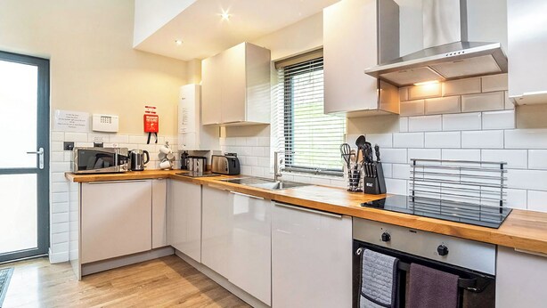 A modern kitchen with white cabinets, a wooden countertop, a built-in oven, and a stainless steel range hood. - 4 Monkbar Mews - UK2693 (York)