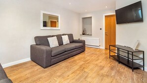 A modern living room with a grey sofa, a flat-screen TV mounted on the wall, and a wooden floor. - 4 Monkbar Mews - UK2693 (York)