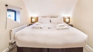 A neatly made bed with towels, a window with a view, and two bedside lamps. - 4 Monkbar Mews - UK2693 (York)