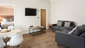 Een moderne woonkamer met een grijze bank, een houten eettafel en een flatscreen televisie die aan de muur is bevestigd.