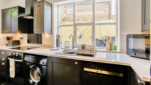 A modern kitchen with a built-in dishwasher, a large window, and a view of a brick wall outside. - 2 bedroom accommodation in Whitby (Whitby)