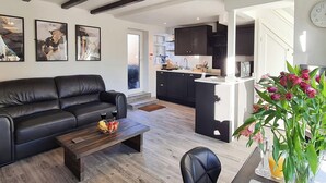 A modern living room with a black leather sofa, a wooden coffee table, and a dining area with a black chair and a white table. - A historical cottage, tucked away in the heart of Whitby’s old town. (Whitby)