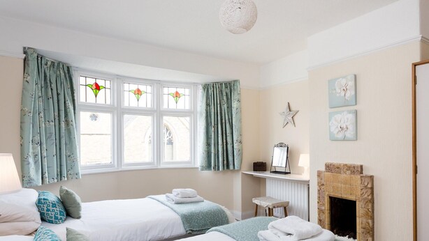 Une chambre d’hôtel avec deux lits, une cheminée, une fenêtre avec des rideaux et une petite table avec une lampe.