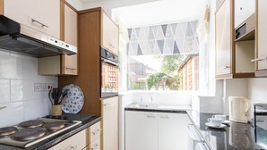 Une cuisine compacte équipée d’une cuisinière à gaz, de meubles blancs, d’une fenêtre donnant sur l’extérieur et d’une machine à café posée sur le plan de travail.