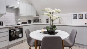 A modern kitchen with white cabinetry, a microwave, a kettle, and a dining area with a round table and two chairs. - Minsters Reach Apartment Four - UK2749 (York)