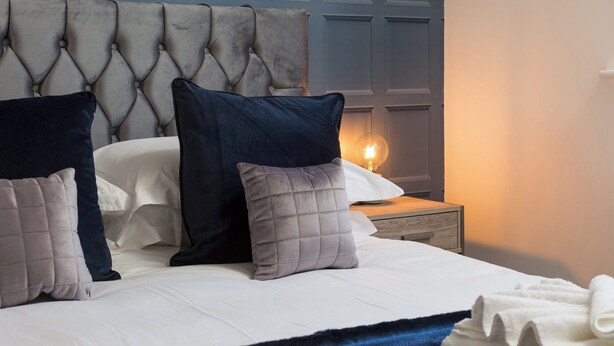 A neatly made bed with a tufted headboard, white linens, and several pillows in shades of grey and navy. - 1 bedroom accommodation in York (York)