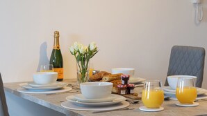 A breakfast table set with plates, bowls, croissants, jams, a bottle of champagne, a vase of flowers, and glasses of orange juice. - 1 bedroom accommodation in York (York)