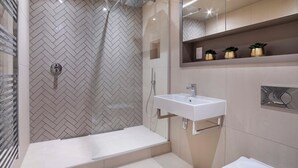 Un baño moderno con pared de baldosas en patrón de espiga, cabina de ducha de vidrio, lavamanos blanco y un inodoro.