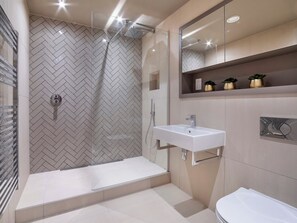 A modern bathroom with a herringbone tile wall, a glass shower enclosure, a white sink, and a toilet. - 1 bedroom accommodation in York (York)