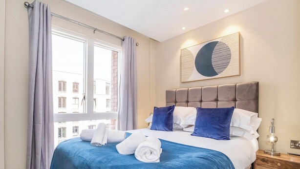 Una habitación de hotel con una cama, una mesita de noche, una lámpara y una ventana con cortinas.