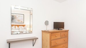 A room with a wooden dresser, a TV on top, a mirror, and a shelf with towels. - Minsters Reach Apartment Two - UK2747 (York)