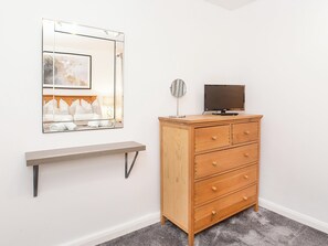 A room with a wooden dresser, a TV on top, a mirror, and a shelf with towels. - Minsters Reach Apartment Two - UK2747 (York)