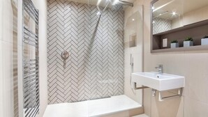 Un bagno moderno con parete rivestita in listelli a spina di pesce, cabina doccia in vetro, lavabo bianco e specchio sopra.