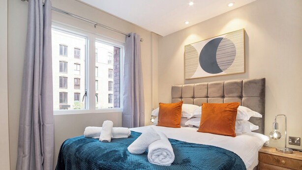 Una camera d'albergo con un letto, una finestra con tende, un'opera d'arte appesa al muro e un comodino con una lampada.