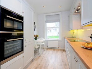 Eine moderne Küche mit weißen Schränken, einem eingebauten Ofen, einem Fenster mit Ausblick und einer Holzausziehtheke mit Gebäck.