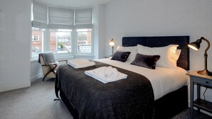 Hotellihuone, jossa on suuri sänky, kaksi yöpöytävalaisinta, tuoli ja ikkuna, josta on näkymä rakennuksiin.