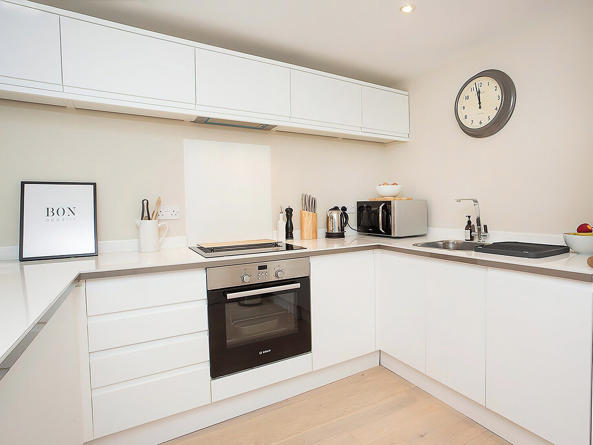 A modern kitchen with white cabinetry, a Bosch oven, a toaster, and a clock on the wall.