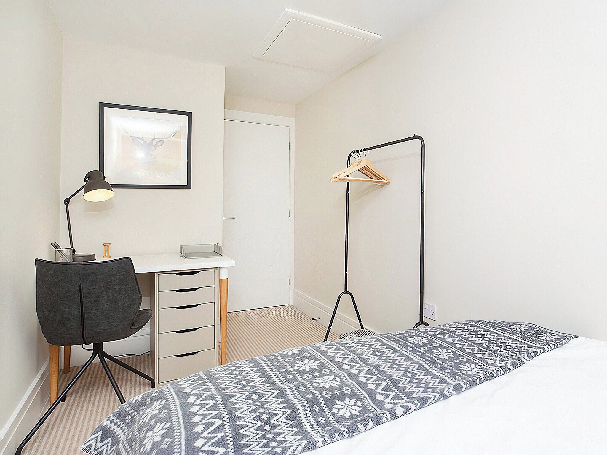A bedroom with a bed, a desk with a chair, a hanging light, and a wardrobe.