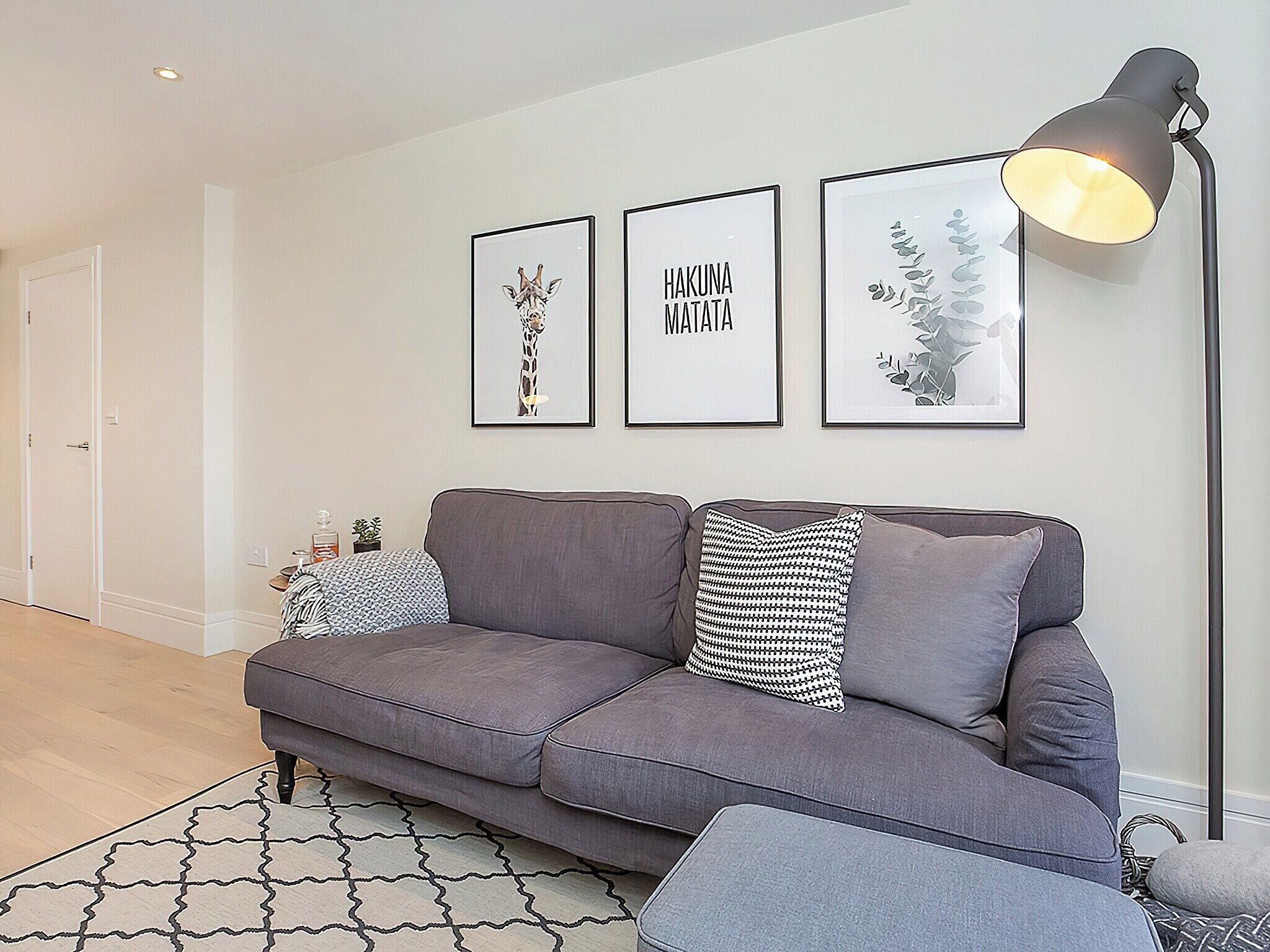 A modern living room with a grey sofa, a patterned rug, and three framed artworks on the wall.