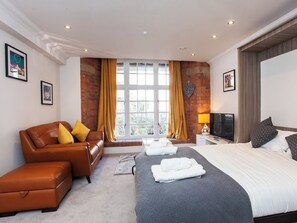 A modern hotel room with a large bed, a sofa, a TV, and a window with curtains. - 1 bedroom accommodation in York (York)