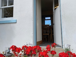 A doorway leading to a room with a window, a wooden chair, and red flowers in the foreground.