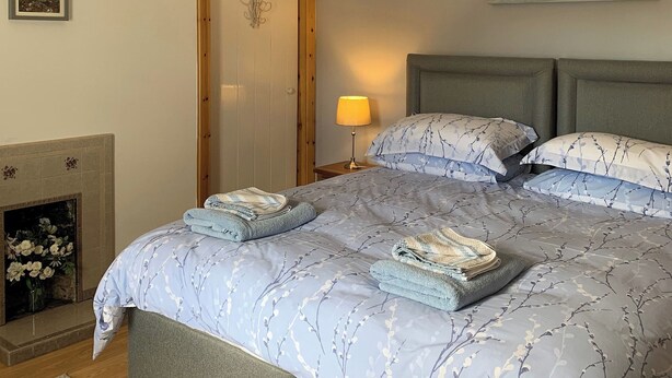 Quarto com cama, mesa de cabeceira, luminária, lareira e duas pinturas na parede.