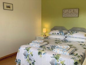 A bedroom with a floral bedspread, two pillows, a bedside lamp, and a framed picture on the wall.
