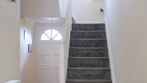 Un escalier dont les marches sont recouvertes de moquette, menant à une porte blanche dotée d’une fenêtre.