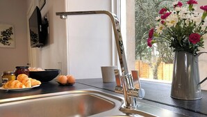Une cuisine dotée d’un évier en acier inoxydable, d’un vase rempli de fleurs et d’une fenêtre donnant sur des arbres.