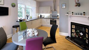Une cuisine moderne avec des armoires blanches, un four encastré et un coin repas comprenant une table ronde et des chaises.