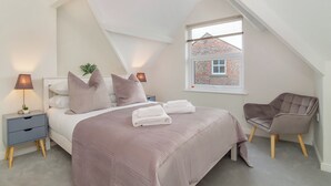 Een slaapkamer met een bed, nachtkastjes, een stoel en een raam met uitzicht op een bakstenen gebouw.
