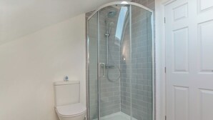 Een badkamer in hoekopstelling met een douche in een glazen cabine, een toilet en een witte deur.
