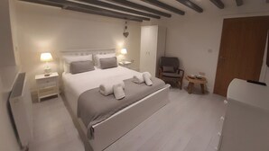 A bedroom with a large bed, bedside tables, a chair, a wardrobe, and a small table with a lamp. - Cottage Apartment - UK2774 (Llandudno)