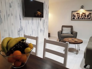 A living room with a TV mounted on the wall, a grey sofa, a wooden coffee table, and a fruit bowl on a table. - Cottage Apartment - UK2774 (Llandudno)