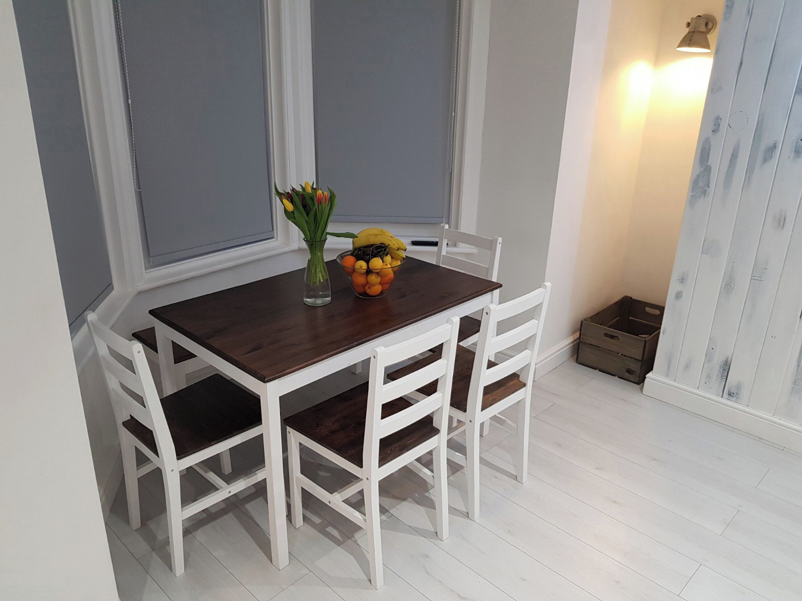 A dining table with white chairs, a vase with flowers, and a bowl of fruit.