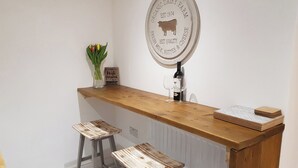 A kitchen area with a wooden countertop, two stools, a wine bottle, and a sign indicating an organic dairy farm. - Cottage Apartment - UK2774 (Llandudno)